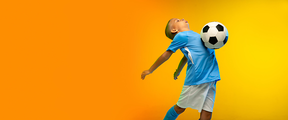 Image showing Young boy as a soccer or football player in sportwear practicing on gradient yellow studio background in neon light