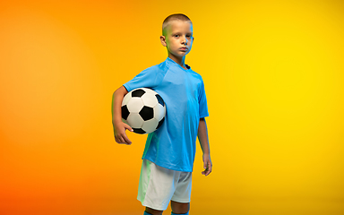 Image showing Young boy as a soccer or football player in sportwear practicing on gradient yellow studio background in neon light