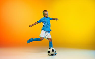 Image showing Young boy as a soccer or football player in sportwear practicing on gradient yellow studio background in neon light