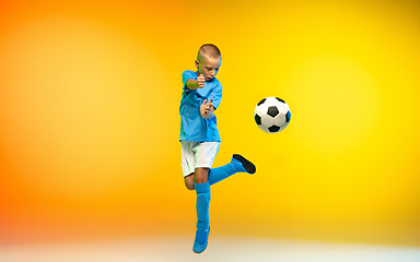 Image showing Young boy as a soccer or football player in sportwear practicing on gradient yellow studio background in neon light