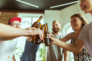 Image showing Young group of friends drinking beer, having fun, laughting and celebrating together. Close up clinking beer bottles