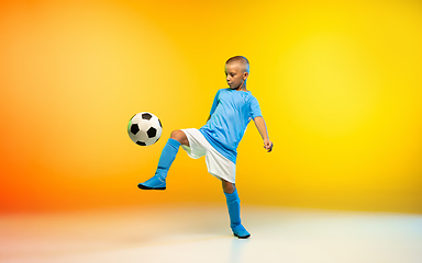 Image showing Young boy as a soccer or football player in sportwear practicing on gradient yellow studio background in neon light