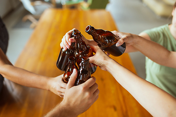 Image showing Young group of friends drinking beer, having fun, laughting and celebrating together. Close up clinking beer bottles