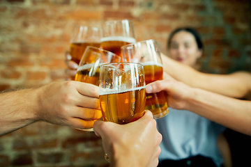 Image showing Young group of friends drinking beer, having fun, laughting and celebrating together. Close up clinking beer glasses