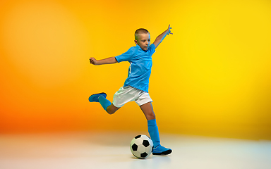 Image showing Young boy as a soccer or football player in sportwear practicing on gradient yellow studio background in neon light