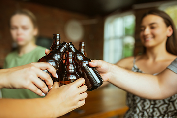 Image showing Young group of friends drinking beer, having fun, laughting and celebrating together. Close up clinking beer bottles