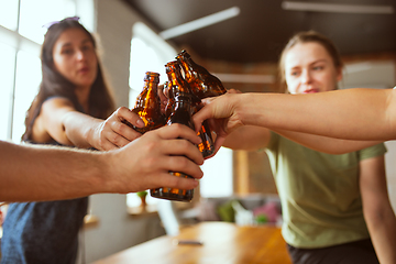 Image showing Young group of friends drinking beer, having fun, laughting and celebrating together. Close up clinking beer bottles