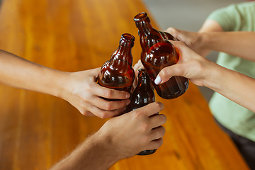 Image showing Young group of friends drinking beer, having fun, laughting and celebrating together. Close up clinking beer bottles