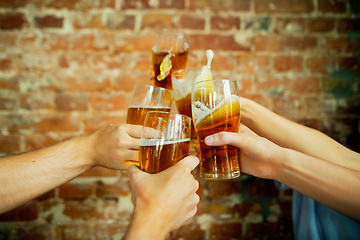 Image showing Young group of friends drinking beer, having fun, laughting and celebrating together. Close up clinking beer glasses