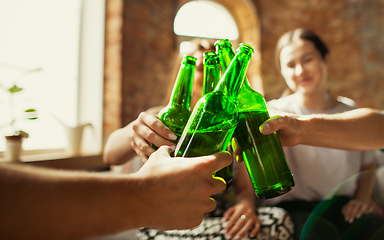 Image showing Young group of friends drinking beer, having fun, laughting and celebrating together. Close up clinking beer bottles