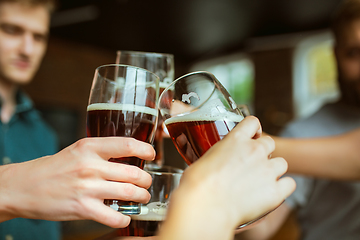 Image showing Young group of friends drinking beer, having fun, laughting and celebrating together. Close up clinking beer glasses