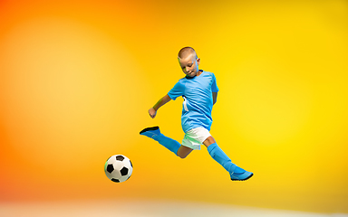 Image showing Young boy as a soccer or football player in sportwear practicing on gradient yellow studio background in neon light