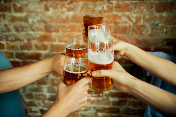 Image showing Young group of friends drinking beer, having fun, laughting and celebrating together. Close up clinking beer glasses