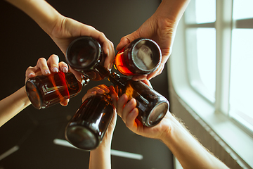 Image showing Young group of friends drinking beer, having fun, laughting and celebrating together. Close up clinking beer bottles