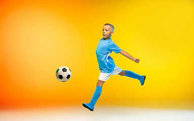 Image showing Young boy as a soccer or football player in sportwear practicing on gradient yellow studio background in neon light