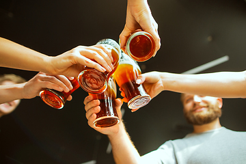 Image showing Young group of friends drinking beer, having fun, laughting and celebrating together. Close up clinking beer glasses