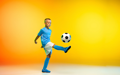 Image showing Young boy as a soccer or football player in sportwear practicing on gradient yellow studio background in neon light