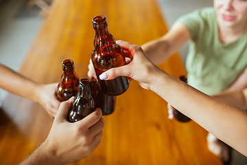 Image showing Young group of friends drinking beer, having fun, laughting and celebrating together. Close up clinking beer bottles