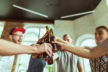 Image showing Young group of friends drinking beer, having fun, laughting and celebrating together. Close up clinking beer bottles