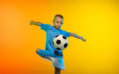 Image showing Young boy as a soccer or football player in sportwear practicing on gradient yellow studio background in neon light