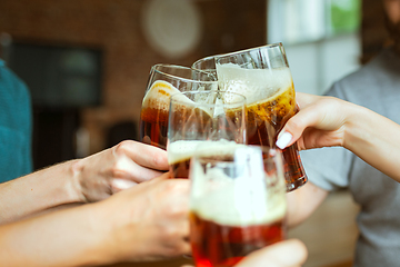 Image showing Young group of friends drinking beer, having fun, laughting and celebrating together. Close up clinking beer glasses