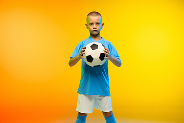 Image showing Young boy as a soccer or football player in sportwear practicing on gradient yellow studio background in neon light