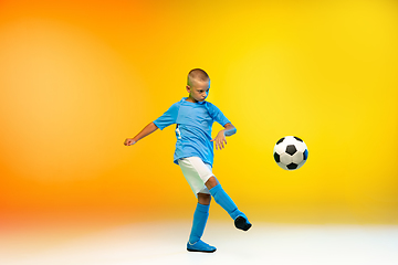 Image showing Young boy as a soccer or football player in sportwear practicing on gradient yellow studio background in neon light