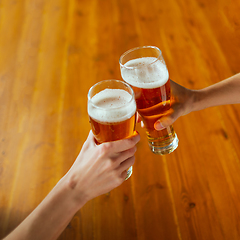 Image showing Young group of friends drinking beer, having fun, laughting and celebrating together. Close up clinking beer glasses