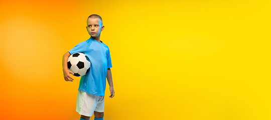 Image showing Young boy as a soccer or football player in sportwear practicing on gradient yellow studio background in neon light