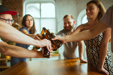 Image showing Young group of friends drinking beer, having fun, laughting and celebrating together. Close up clinking beer bottles