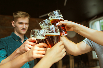 Image showing Young group of friends drinking beer, having fun, laughting and celebrating together. Close up clinking beer glasses