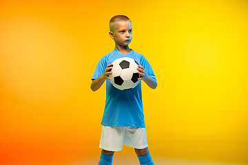 Image showing Young boy as a soccer or football player in sportwear practicing on gradient yellow studio background in neon light