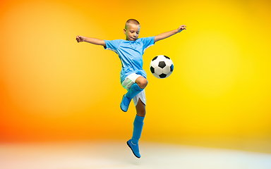 Image showing Young boy as a soccer or football player in sportwear practicing on gradient yellow studio background in neon light