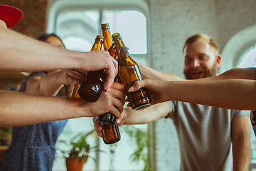 Image showing Young group of friends drinking beer, having fun, laughting and celebrating together. Close up clinking beer bottles