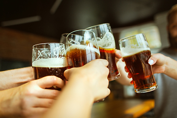 Image showing Young group of friends drinking beer, having fun, laughting and celebrating together. Close up clinking beer glasses