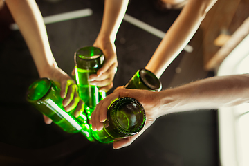 Image showing Young group of friends drinking beer, having fun, laughting and celebrating together. Close up clinking beer bottles