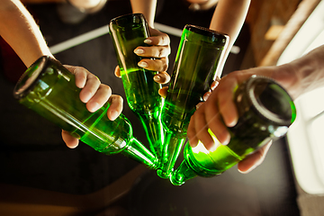 Image showing Young group of friends drinking beer, having fun, laughting and celebrating together. Close up clinking beer bottles