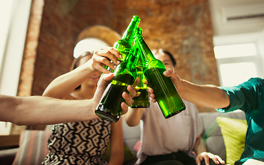 Image showing Young group of friends drinking beer, having fun, laughting and celebrating together. Close up clinking beer bottles