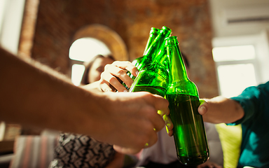 Image showing Young group of friends drinking beer, having fun, laughting and celebrating together. Close up clinking beer bottles