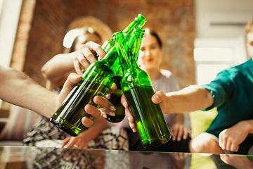 Image showing Young group of friends drinking beer, having fun, laughting and celebrating together. Close up clinking beer bottles