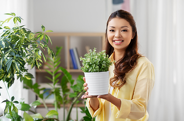 Image showing happy asian woman with flower in pot at home