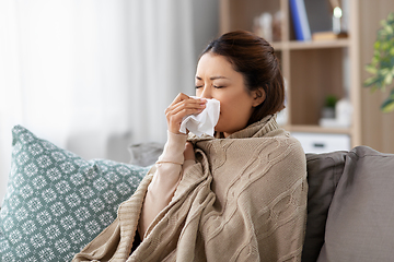 Image showing sick asian woman blowing nose with tissue at home
