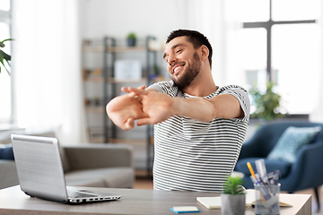 Image showing happy man with laptop stretching at home office