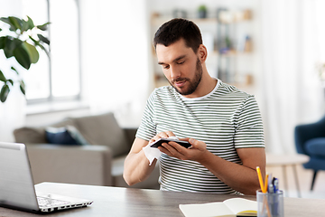 Image showing man cleaning phone with wet wipe at home office