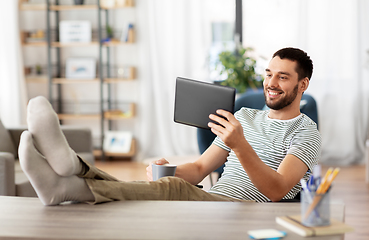 Image showing man with tablet pc resting feet on table at home