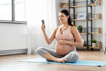 Image showing happy pregnant woman with phone doing yoga at home