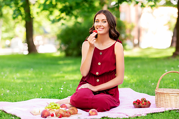 Image showing happy woman eating strawberry on picnic at park