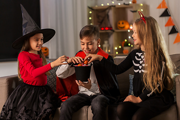 Image showing kids in halloween costumes sharing candies at home