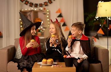 Image showing kids in halloween costumes eating cupcakes at home