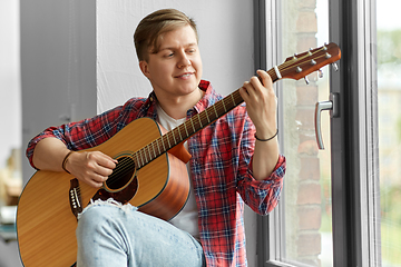 Image showing young man playing guitar sitting on windowsill